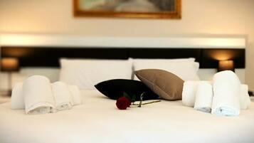 Ein ordentlich bezogenes Bett mit aufgerollten Handtüchern, einem schwarzen Kissen, einem braunen Kissen und einer einzelnen roten Rose.
