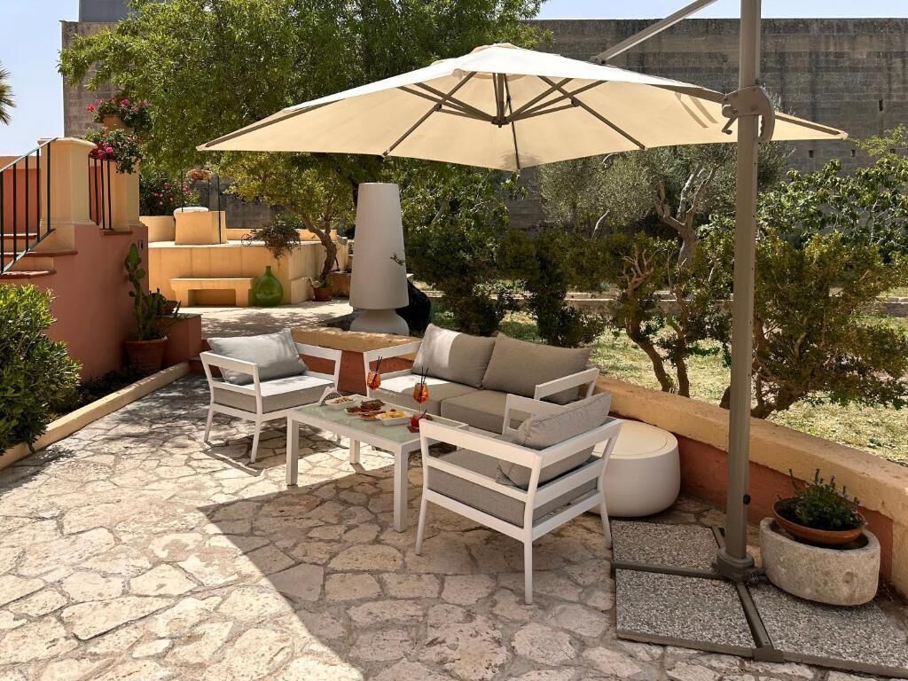 An outdoor patio with a beige umbrella, white furniture, and potted plants.