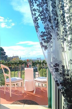 A balcony with two white chairs and a table, a glass of wine, and a view of the cityscape.