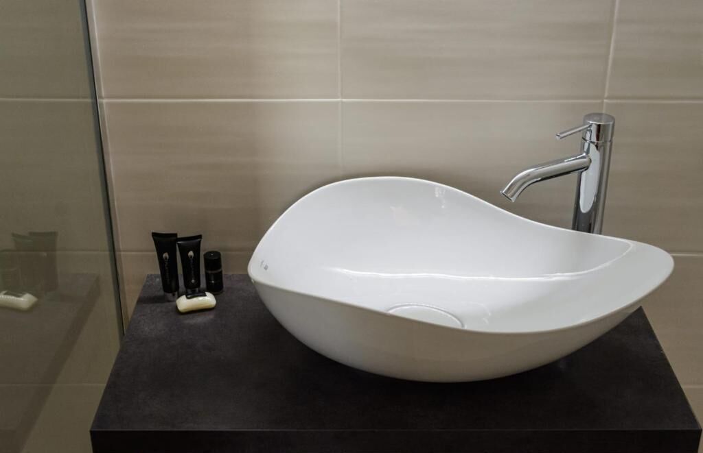 A modern bathroom with a large, white vessel sink, a sleek chrome faucet, and a dark countertop.