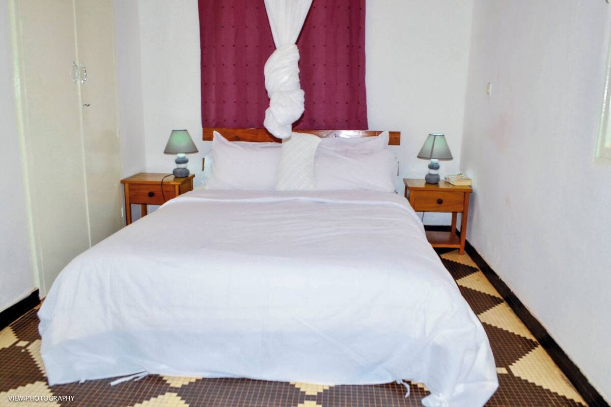 A neatly made bed with white linens, two bedside tables with lamps, and a patterned floor.