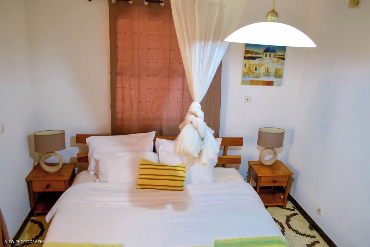 A hotel room with a bed, two bedside tables with lamps, a curtain, and a wall-mounted painting.
