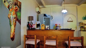 A bar area with wooden chairs, a painting of a zebra, a clock, and a refrigerator with a 'SIKA' sign. - Umoja Guesthouse II (Ouagadougou)