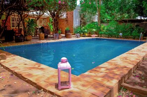A rectangular swimming pool with a brick border, surrounded by potted plants and outdoor furniture.