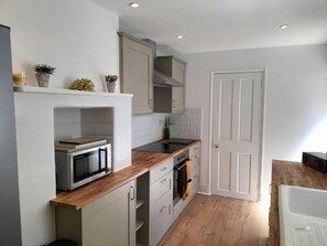 Compact kitchen with microwave, stove, and sink, featuring wooden countertops and cabinetry.