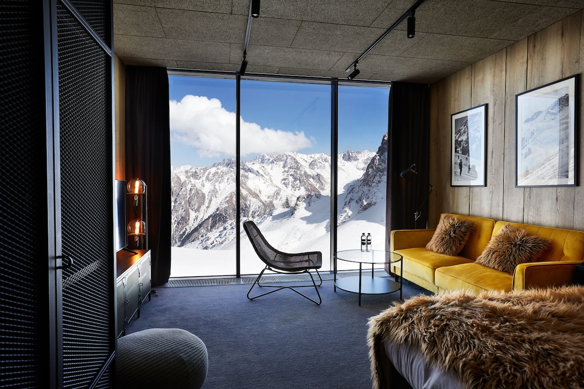 A modern room with a large window offering a mountain view, a yellow sofa, and a fur throw.