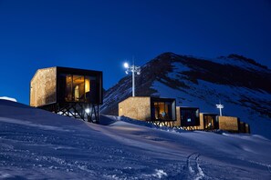 A snow-covered landscape with a modern building featuring glass windows and a wooden exterior.
