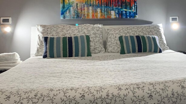 A bed with floral-patterned bedding and striped pillows, a colorful abstract painting above it, and two wall-mounted light switches. - B&B Residence Armonia Sulmona, city center (Sulmona)