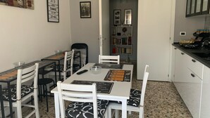 A dining area with a long table, white chairs, and a black and white patterned cushion. There is a bookshelf with books and decorative items in the background. - B&B Residence Armonia Sulmona, city center (Sulmona)