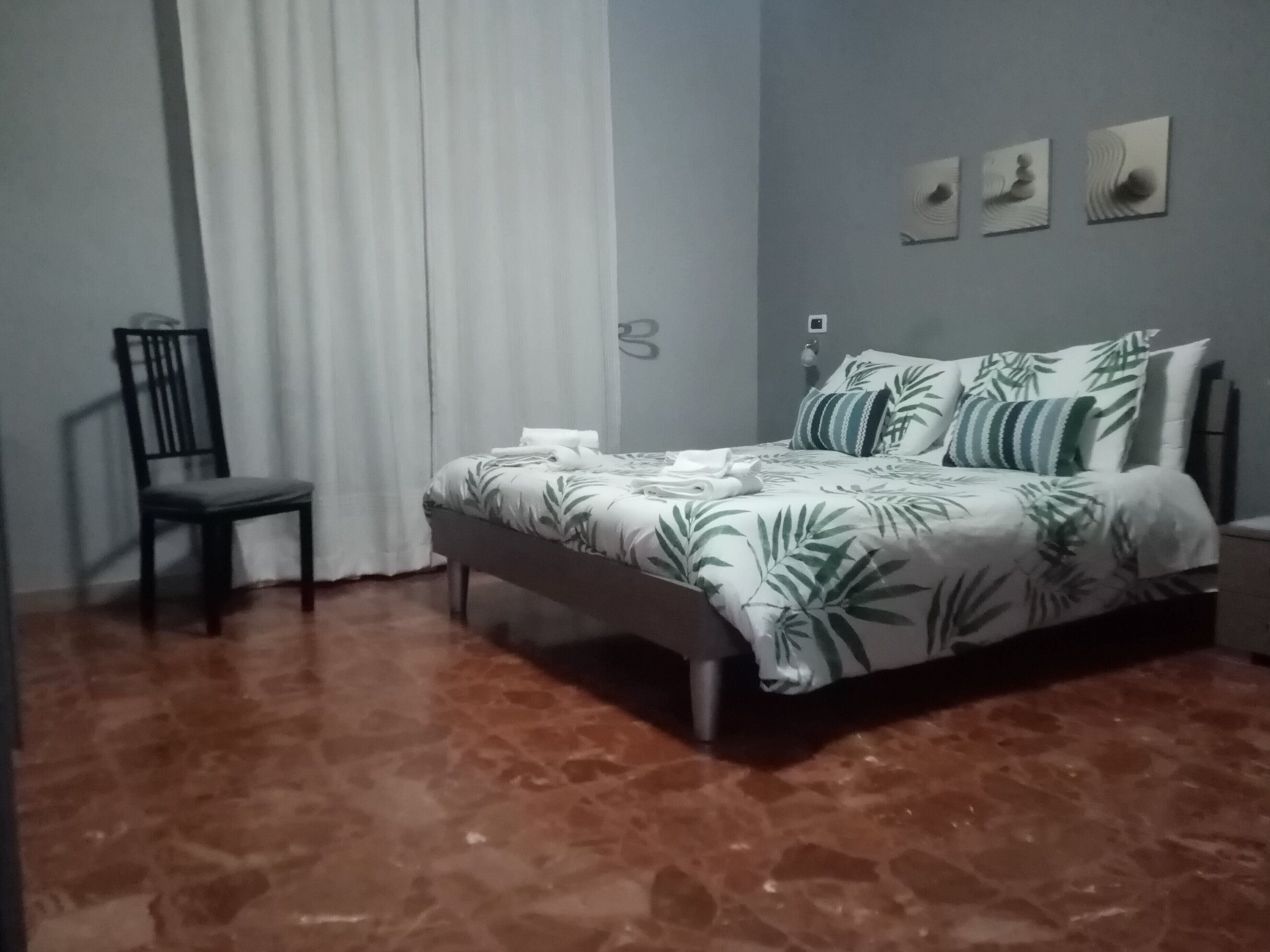Una camera da letto con un letto, una sedia, un comodino e una parete decorata con tre quadri.