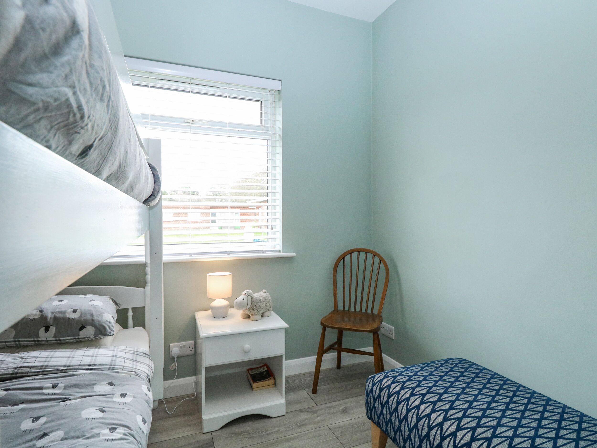 A child's bedroom with a bunk bed, a desk with a lamp, and a chair.