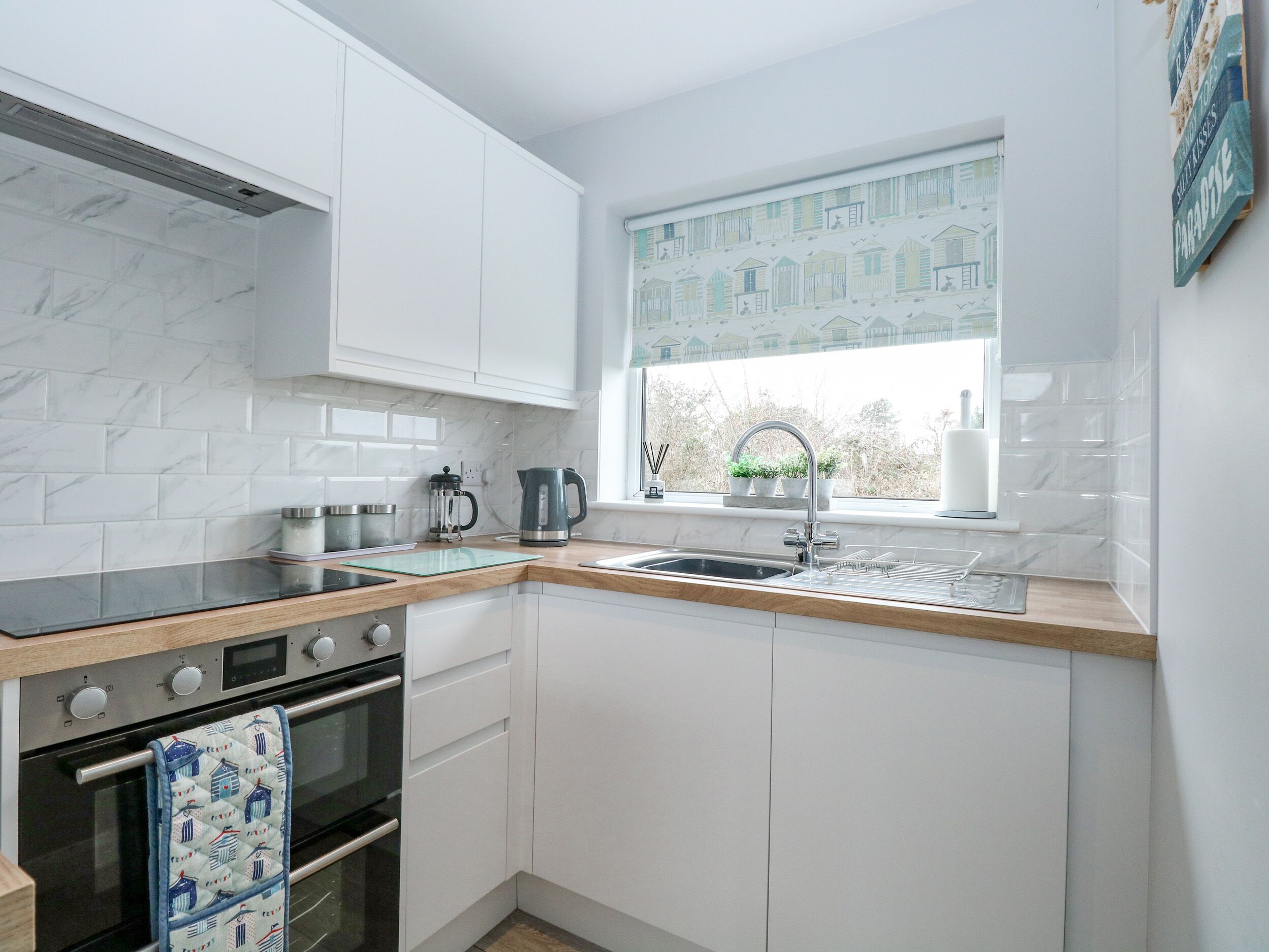 Een moderne keuken met witte kasten, een houten aanrecht, een ingebouwde oven en een raam met uitzicht op huizen.