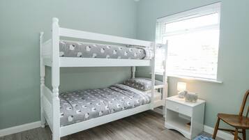 A bunk bed with grey and white patterned bedding, a small bedside table with a lamp, and a window with blinds.