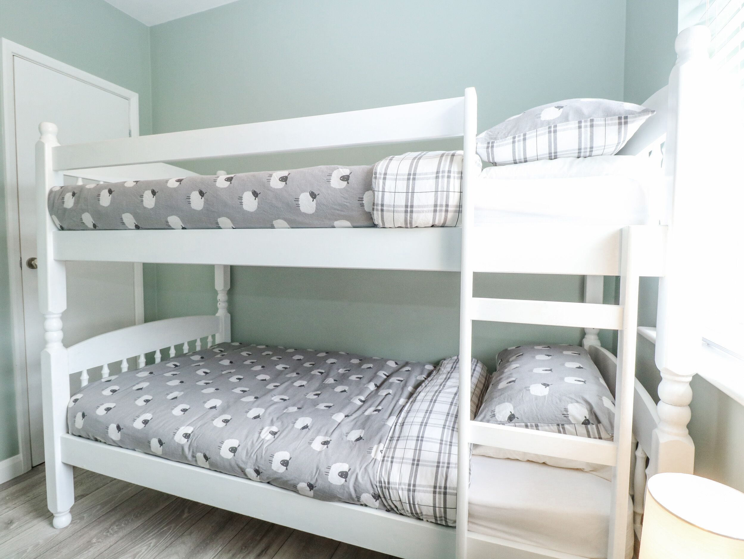 A bunk bed with grey and white bedding, a plaid pillow, and a white door in the background.