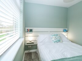 Un dormitorio con cama, mesitas de noche, ventana con persianas y vistas al exterior a zonas verdes.