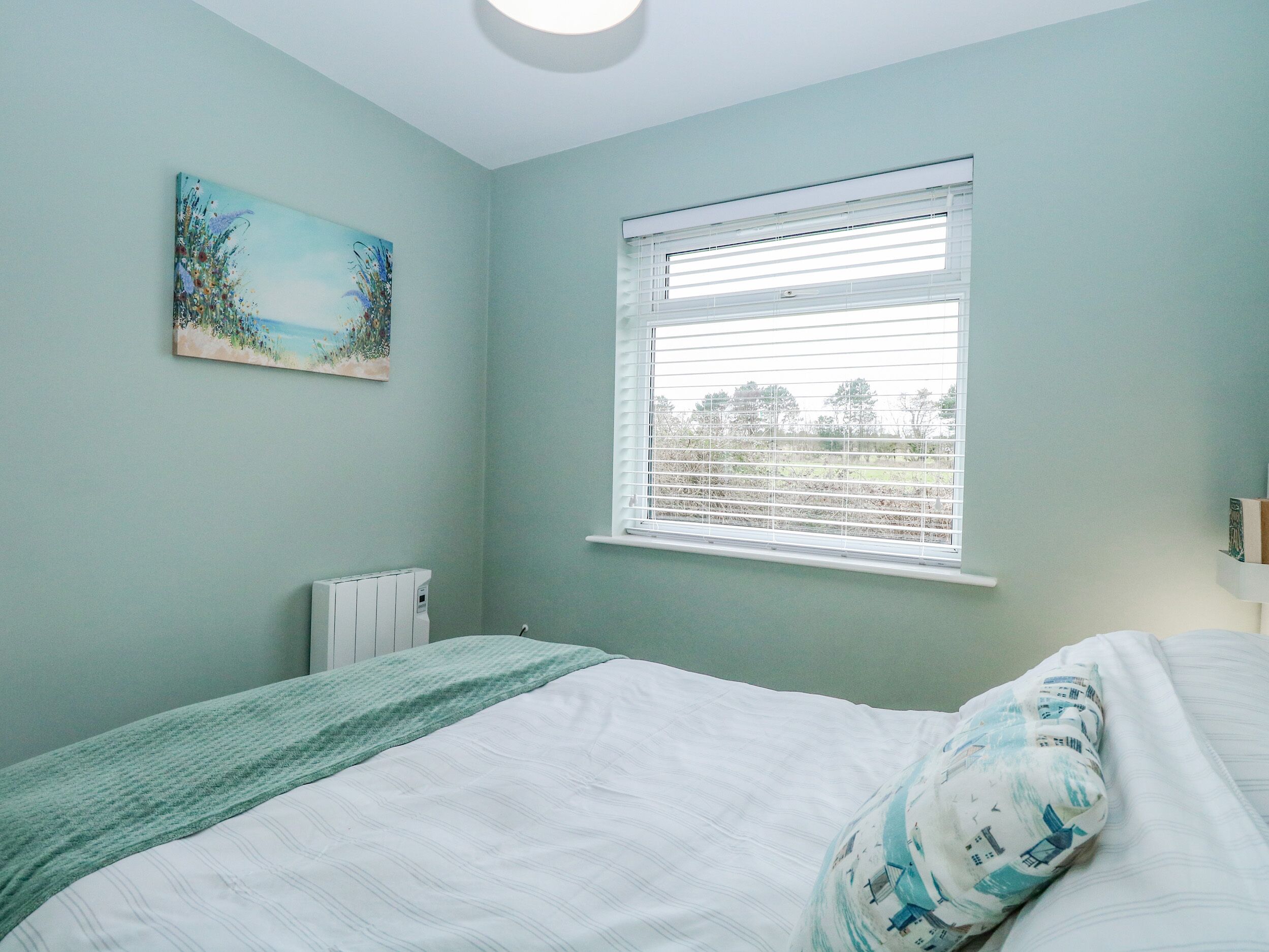 A bedroom with a bed, a radiator, a window with blinds, and a painting on the wall.