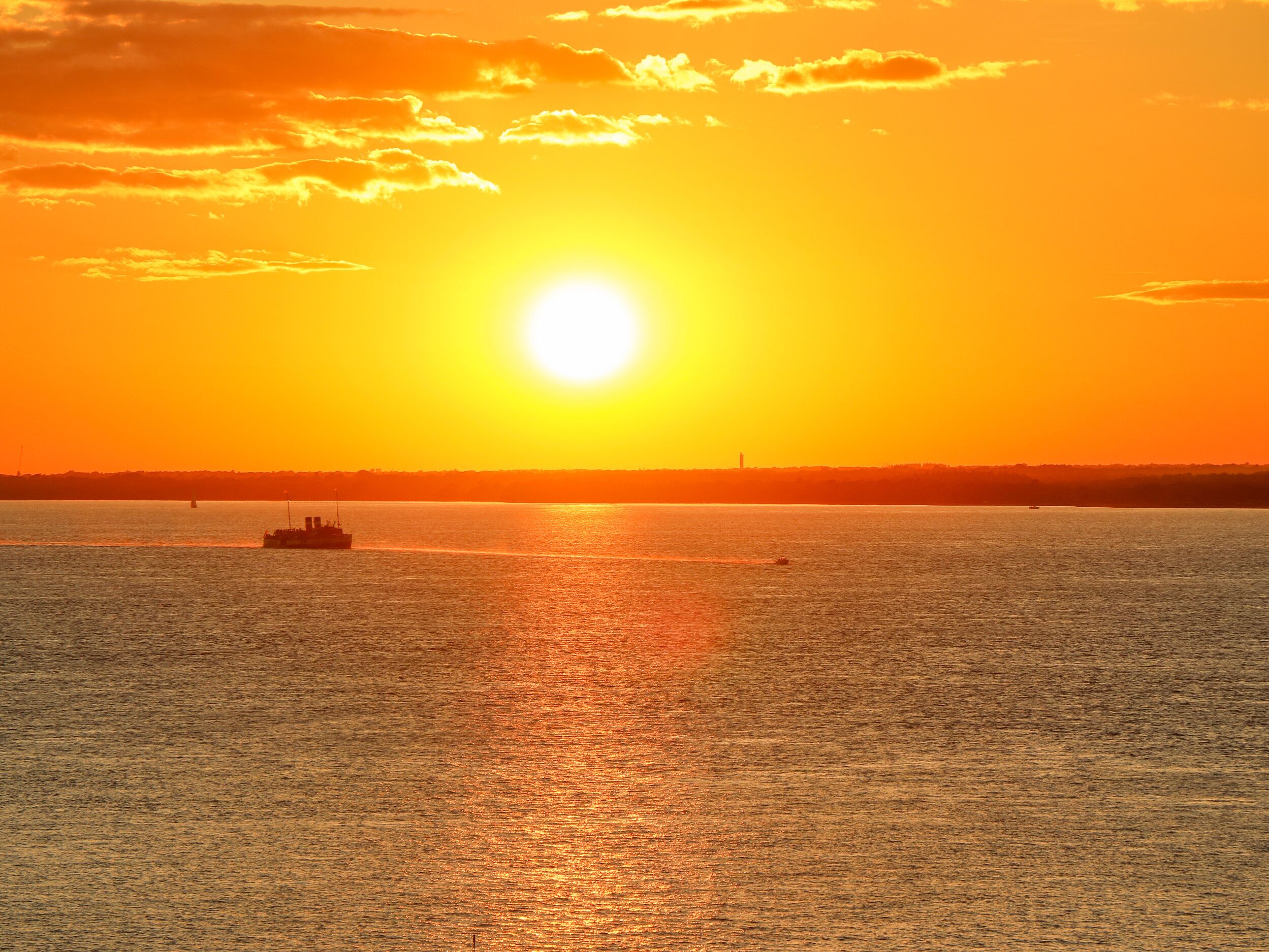 A sunset over a calm body of water with a boat in the foreground.
