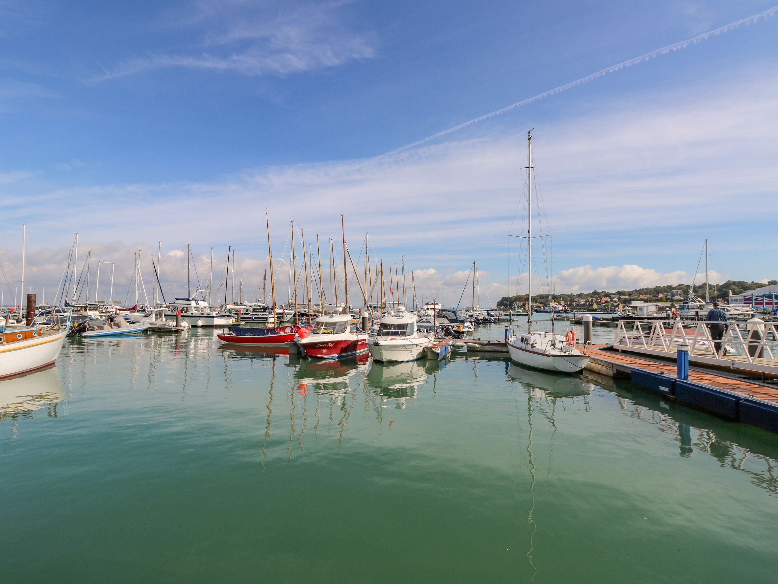 A marina with multiple boats docked, calm water, and a clear sky.