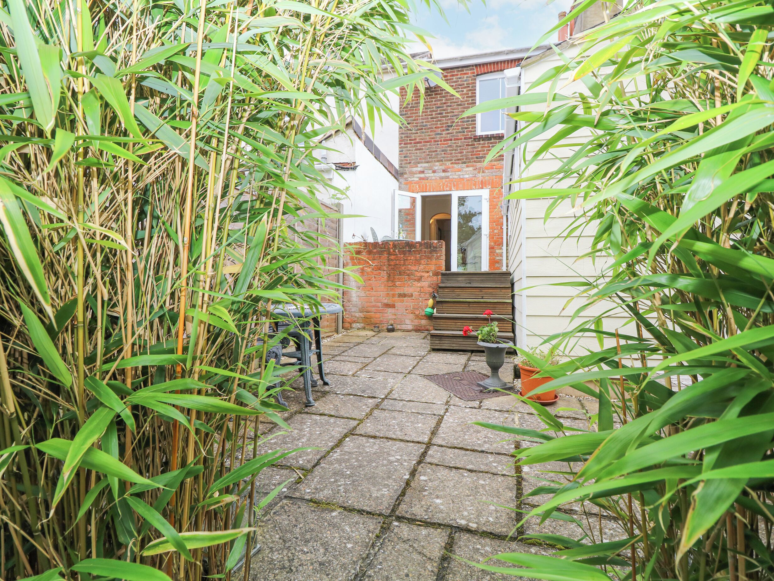 A narrow pathway leading to a brick house with a small front porch.