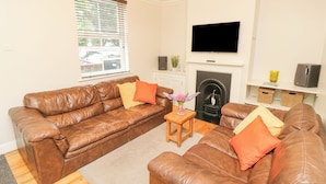 A living room with a brown leather sofa, a wooden coffee table, and a fireplace. - Seagulls Perch (Cowes)