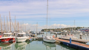 A marina with various boats docked, a pier, and a building with a Union Jack flag in the background. - Seagulls Perch (Cowes)
