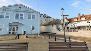 A blue building labeled "Cowes Harbour Commission" with a street lamp and benches in the foreground. - Seagulls Perch (Cowes)