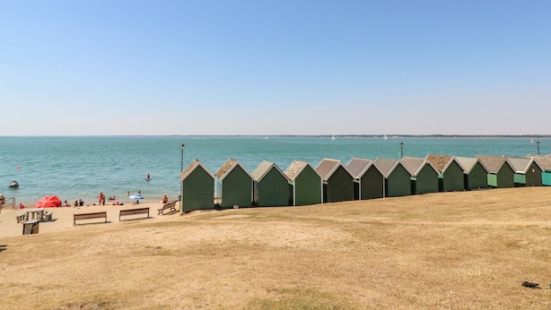 A beach with green beach huts, a sandy area with benches, and the sea in the background. - Seagulls Perch (Cowes)
