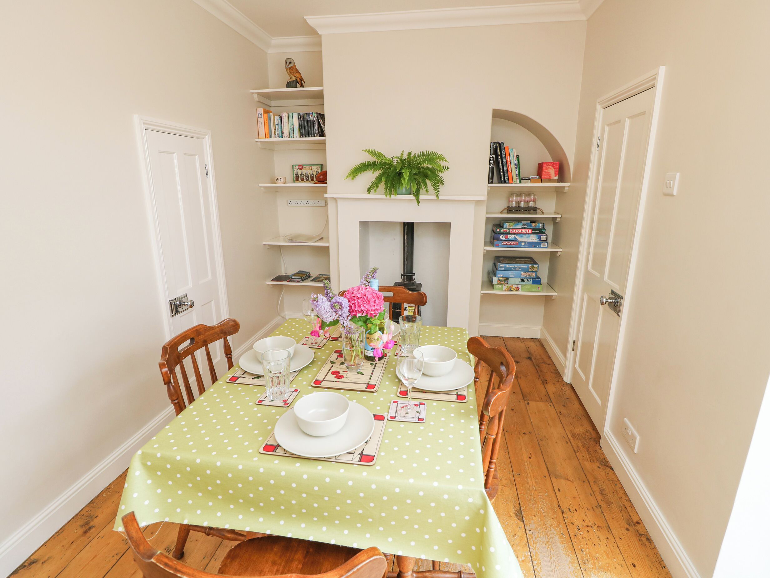 A dining room with a green polka dot tablecloth, wooden chairs, and a white fireplace.
