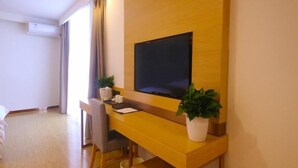 Ein Hotelzimmer mit Holztisch, Flachbildfernseher, Sessel, kleiner Topfpflanze und Bett.