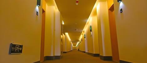 A hotel corridor with directional signs, a fire alarm, and a patterned carpet.