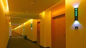 Ein Hotelgang mit Türen, einem Mülleimer und beleuchteten Schildern.