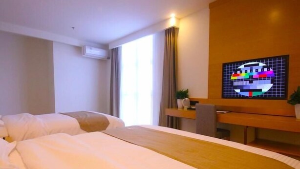 Ein Hotelzimmer mit zwei Betten, einem Schreibtisch, einem Fernseher und einem Fenster mit Vorhängen.