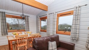 Ein gemütliches Zimmer mit braunem Ledersofa, einem Holzesstisch mit Stühlen und karierten Vorhängen an den Fenstern.