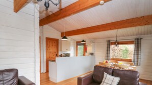Ein Ferienhaus-Interieur mit Holzboden, einem braunen Ledersofa, einer Küchenzeile und einem Esstisch mit Stühlen.