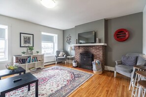 Una sala de estar con chimenea, televisor, estantería y mesa de centro.