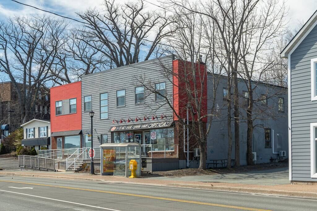 A two-story building with a storefront, a bus stop, and a sidewalk.