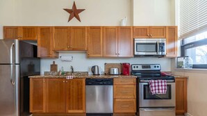 A kitchen with wooden cabinets, a stainless steel refrigerator, a dishwasher, a microwave, a stove, and a star decoration on the wall. - Spacious Downtown Loft with AC (Halifax)
