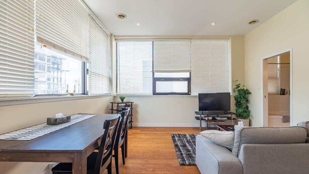 A modern living room with a dining table, sofa, TV, and large windows with blinds. - Spacious Downtown Loft with AC (Halifax)