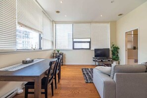A modern living room with a dining table, sofa, TV, and large windows with blinds. - Spacious Downtown Loft with AC (Halifax)