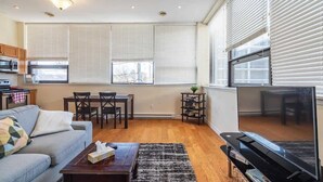 A living room with a sofa, coffee table, TV, and dining area. - Spacious Downtown Loft with AC (Halifax)