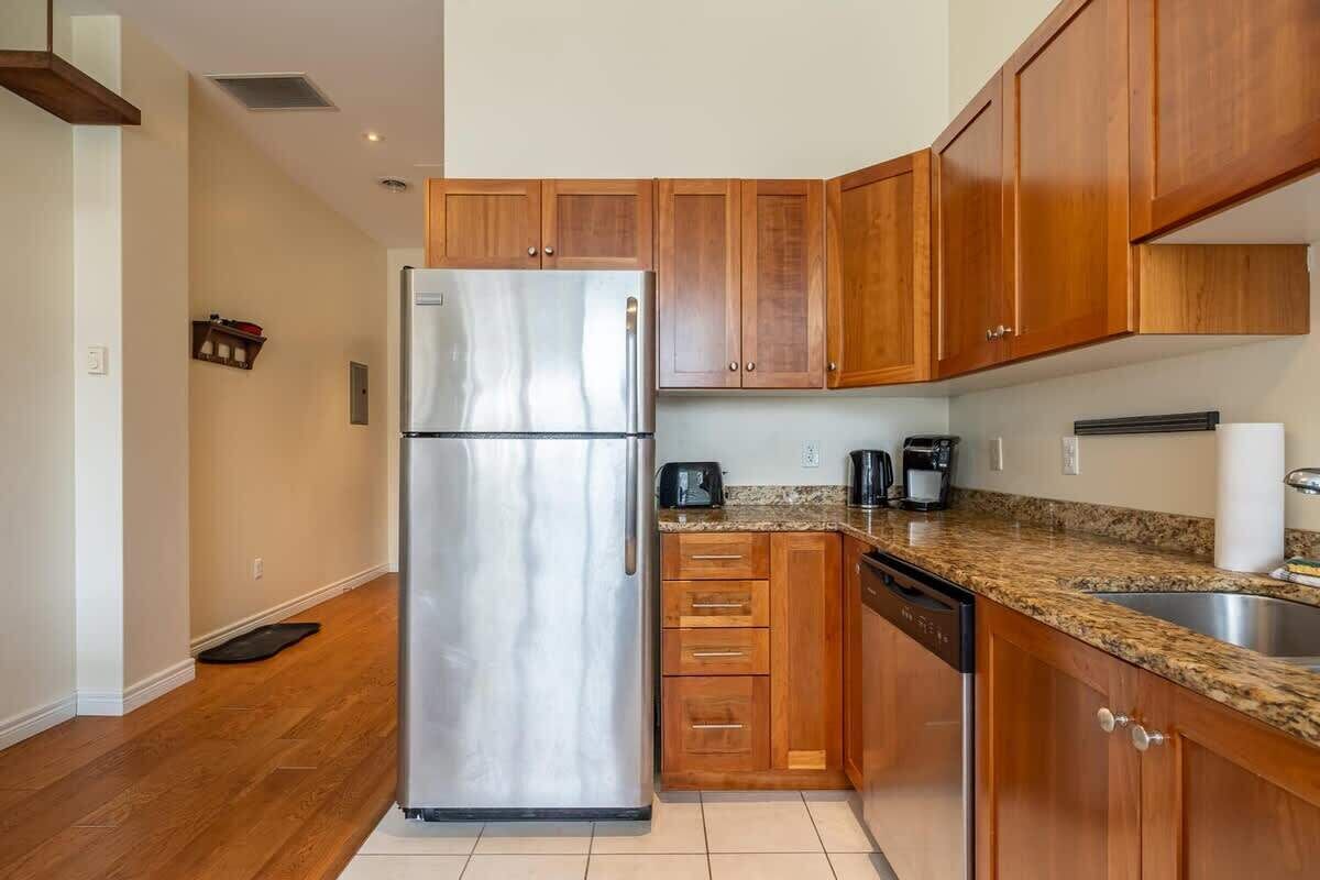 A kitchen with wooden cabinets, a stainless steel refrigerator, a dishwasher, and a granite countertop.