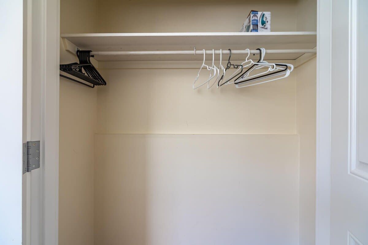 A closet with a white door, a shelf with a box, and a row of hangers.