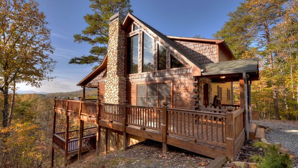 A cabin with a stone chimney, large windows, and a wooden deck.