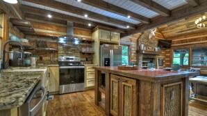 Une cuisine rustique avec des meubles en bois, un grand îlot central, des appareils électroménagers en acier inoxydable et une cheminée en pierre.
