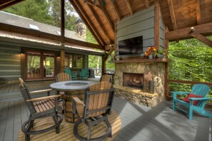 A wooden deck with a stone fireplace, outdoor seating, and a TV mounted on the wall. - Cozy Creek welcomes pets to its tranquil waters, offering fishing, swimming, a hot tub, outdoor fireplace, fire-pit, and WiFi (Epworth)