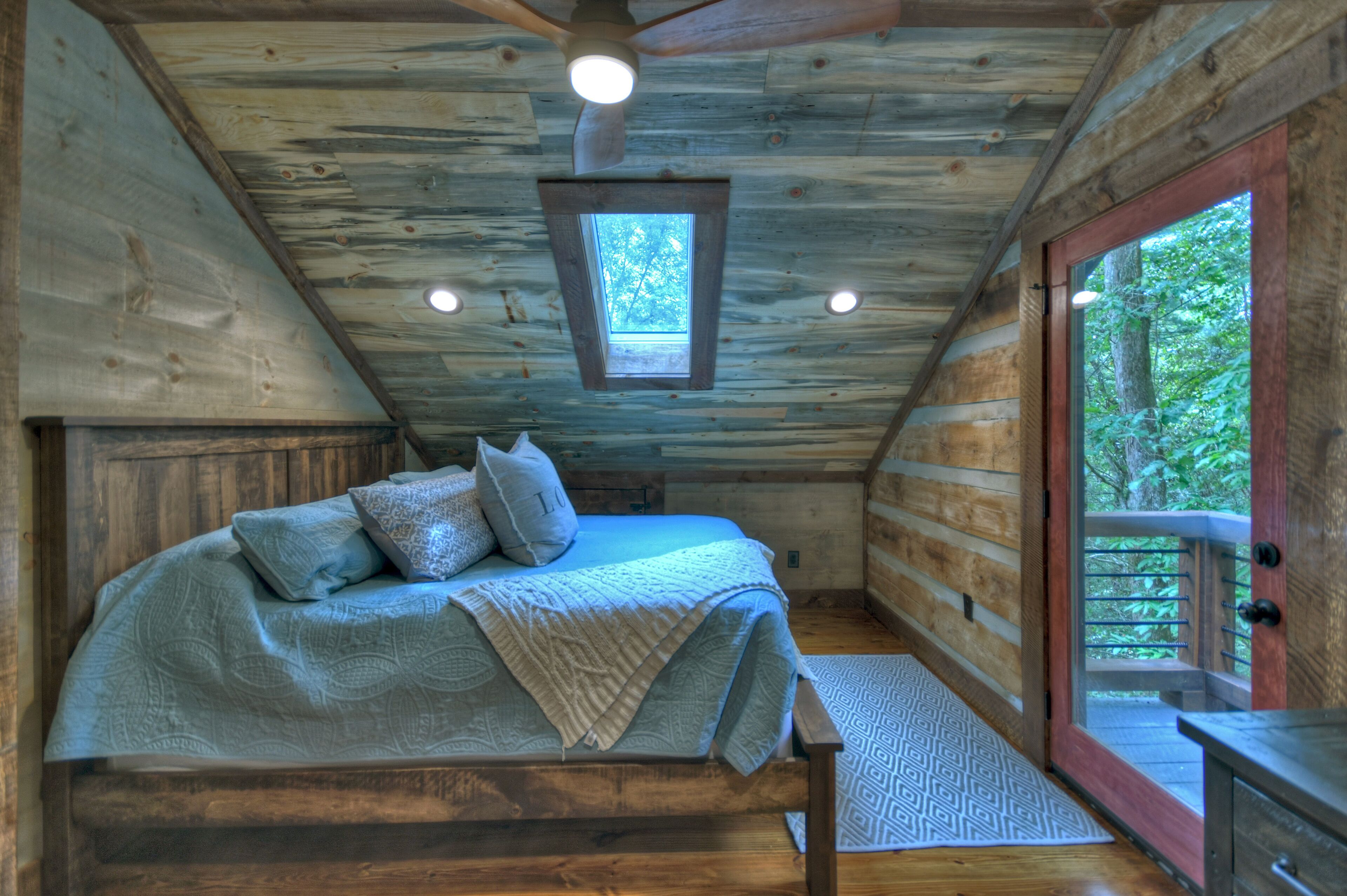 A log cabin bedroom with a bed, pillows, a window, and a door leading to an outdoor deck.