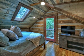 A log cabin bedroom with a bed, pillows, a TV, a wooden dresser, a ceiling fan, and a skylight. - Cozy Creek welcomes pets to its tranquil waters, offering fishing, swimming, a hot tub, outdoor fireplace, fire-pit, and WiFi (Epworth)
