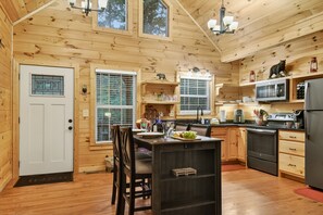 A wooden cabin interior with a kitchen, dining area, and a door with a window.