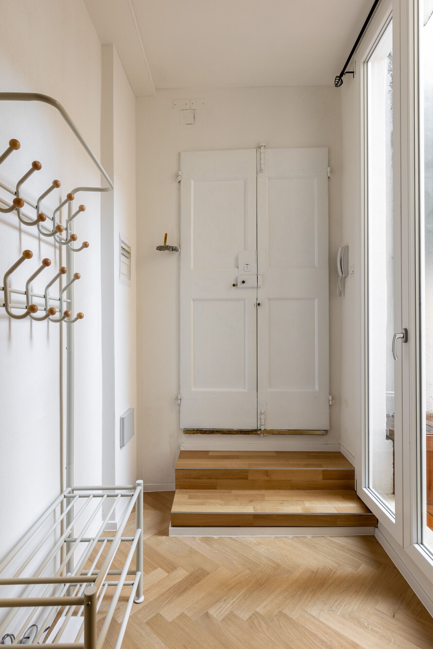A hallway with a white door, a coat rack, and a wooden floor.