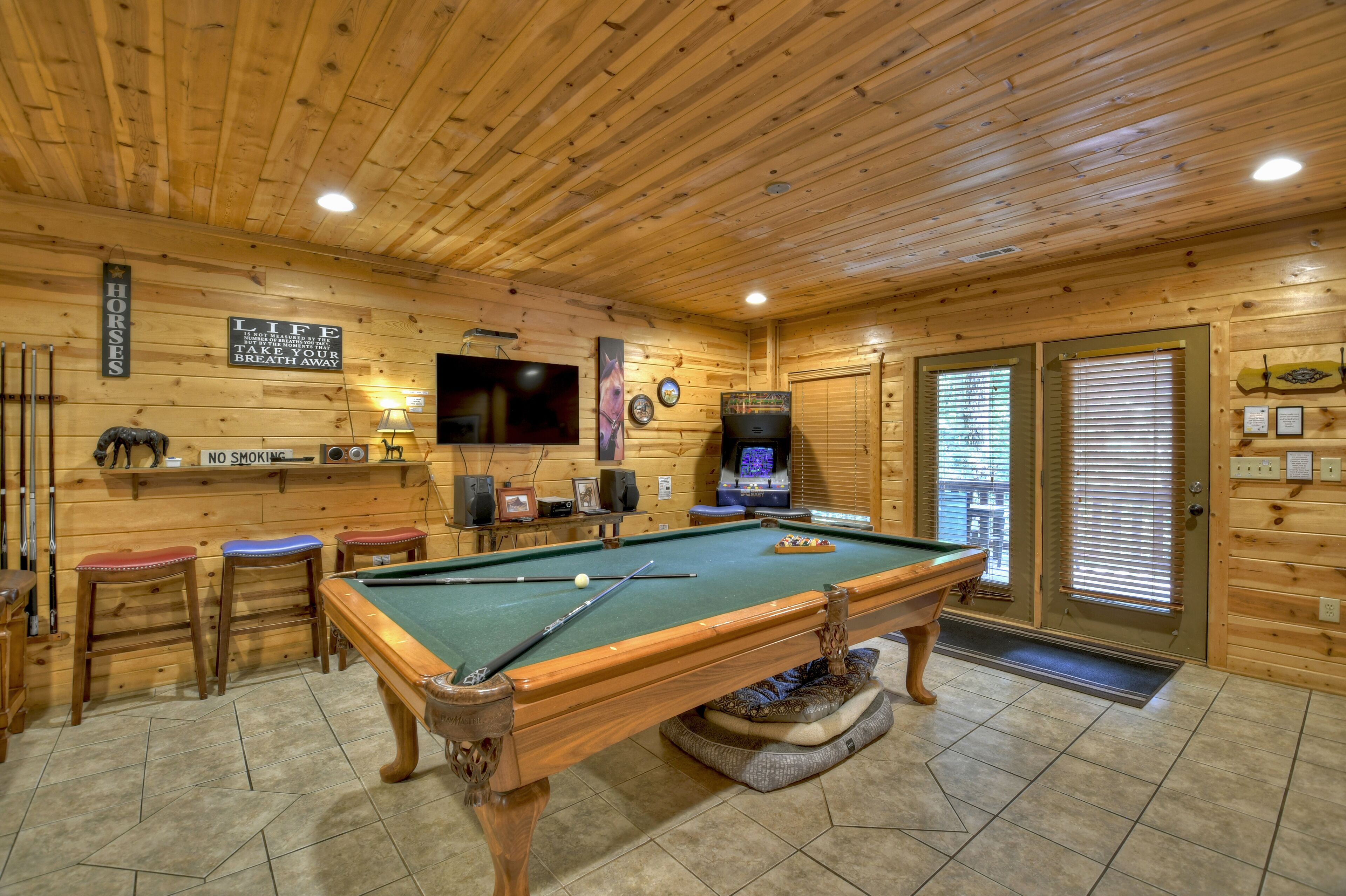 A pool table in a wooden room with a television, a no smoking sign, and a clock on the wall.
